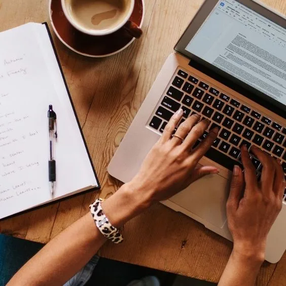 hands typing on a laptop and a book beside it